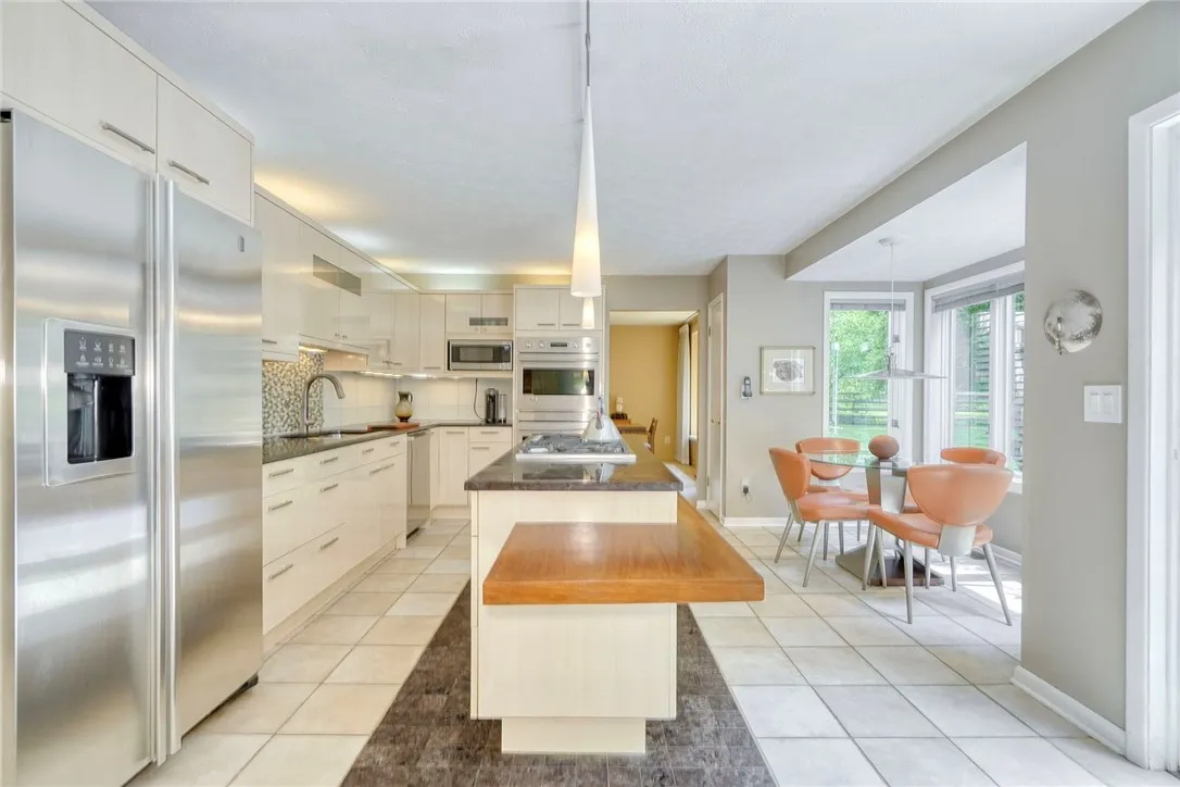 UPDATED DESIGNER KITCHEN with statement island, gas cooktop, granite counters, tile backsplash, quality cabinetry, and bright eat-in nook overlooking backyard.