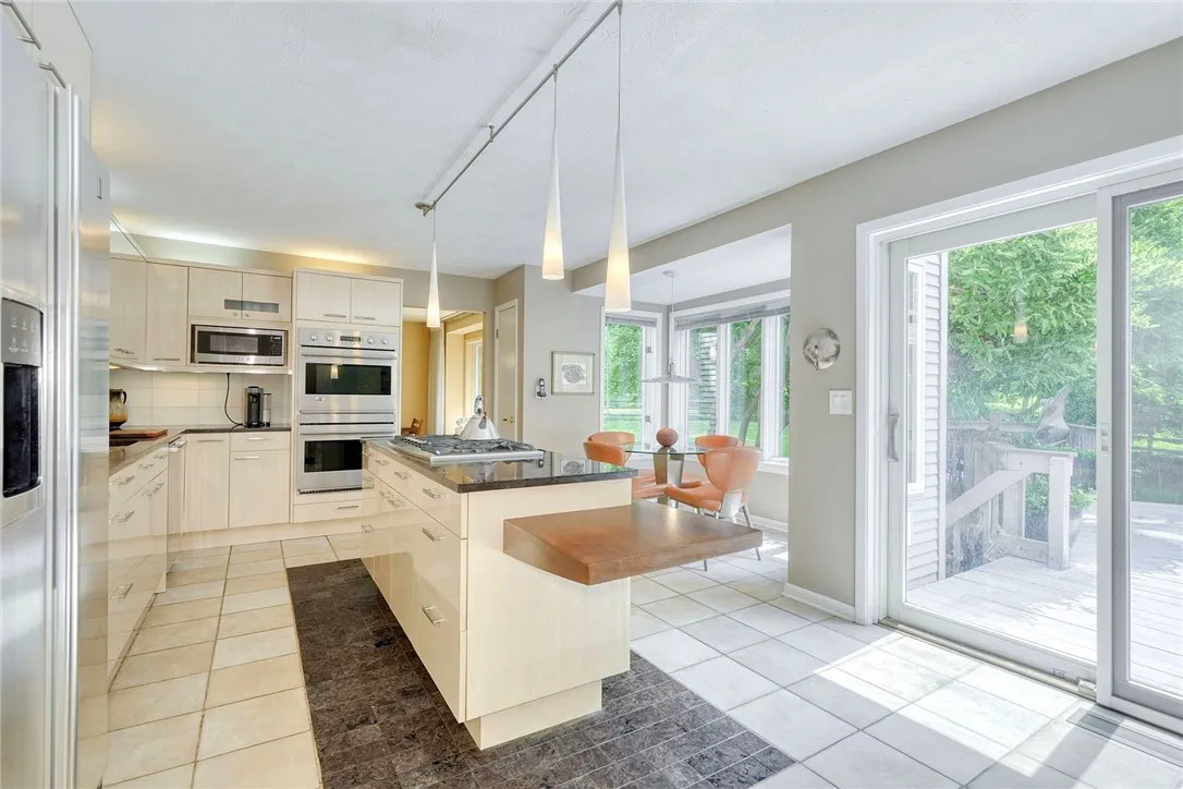 UPDATED DESIGNER KITCHEN with statement island, gas cooktop, granite counters, tile backsplash, quality cabinetry, and bright eat-in nook overlooking backyard.