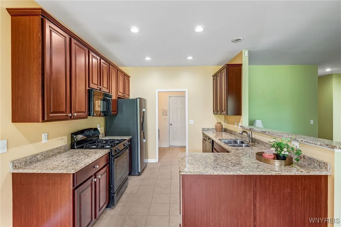 Rich wood cabinets and recess lighting with view of the living room and large eat in area. Ceramic tile flooring.