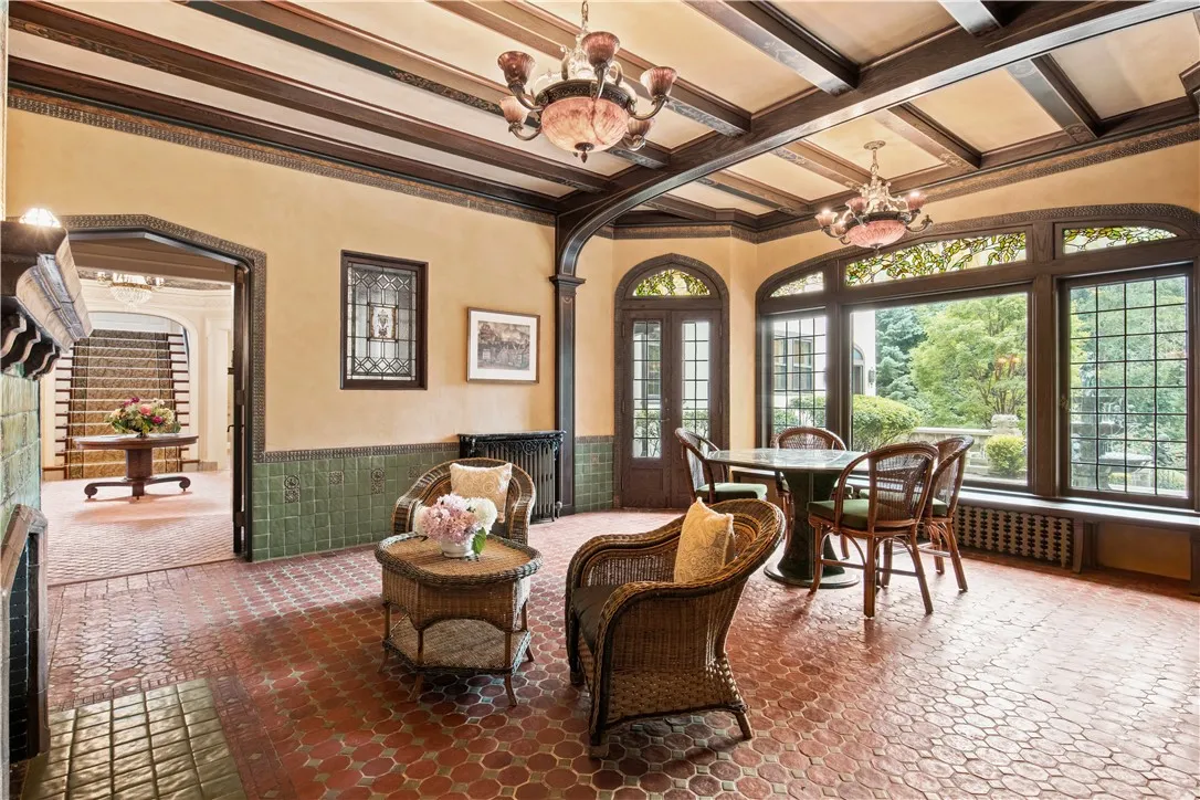 The conservatory features acid-wash tile restoration, French beams, an ornamental Hartford Faience fireplace, a coral glass and iron chandelier, a wall fountain, original sconces with mica stone shades, and phenomenal views of the lush grounds.