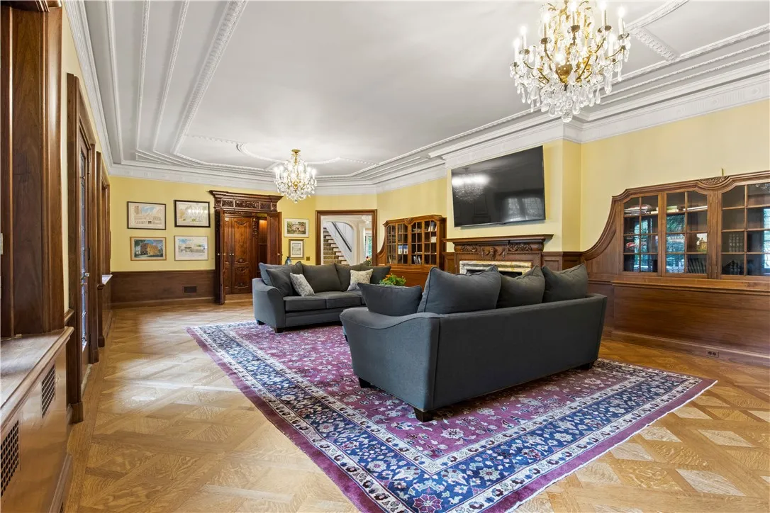 The ballroom, features blonde parquet floor, built-in display cabinets, dual chandeliers, and twin carved doors. Leaded glass windows and doors offer views of the tile and stone patio and a stone fountain, creating an exquisite entertaining space.