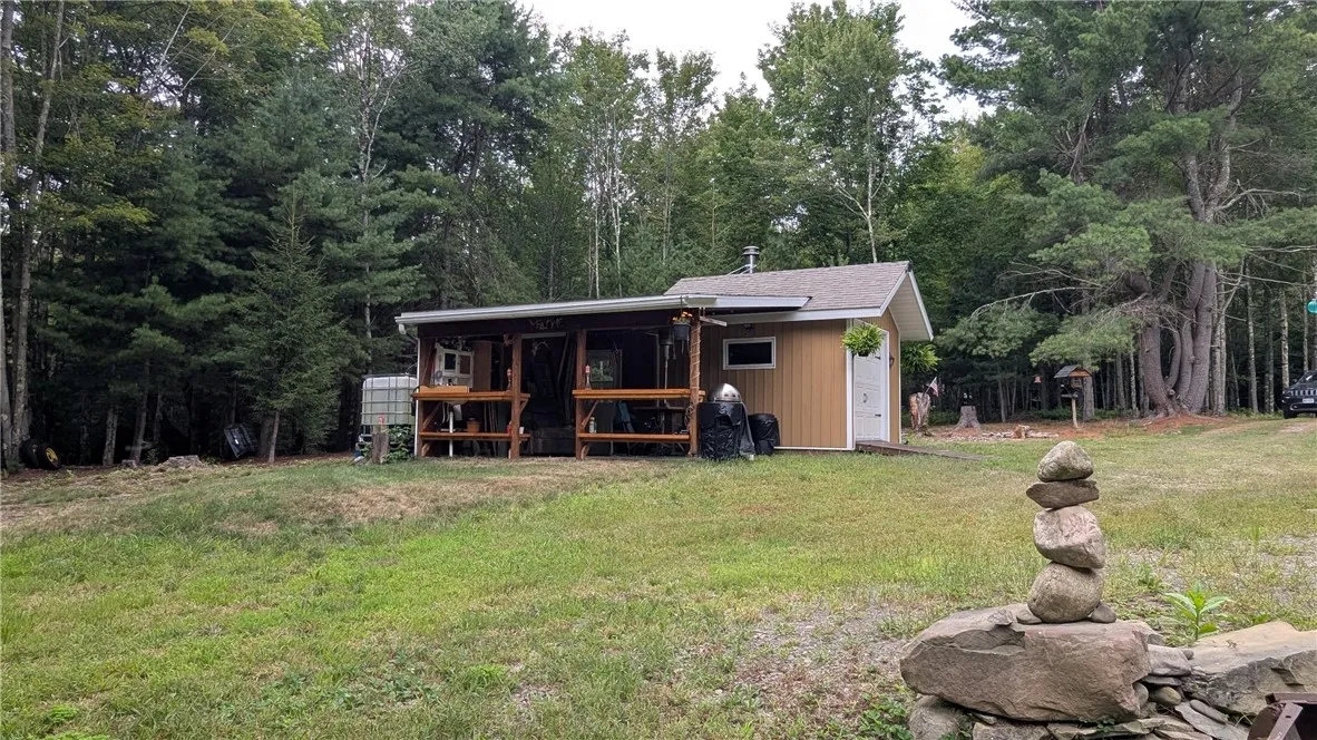Distant view shows shed with addition. behind shed is water collection system that supplies sink. Shed has generator that supplies power. Generator is offered for sale as well