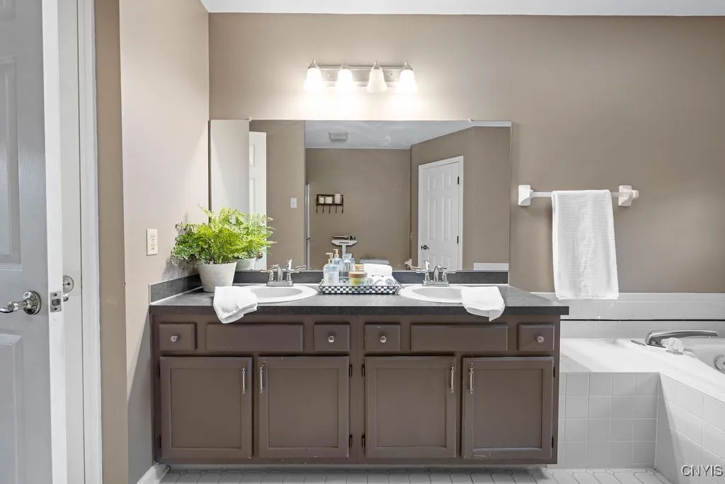 Primary bathroom with dual sinks, tile flooring, soaking tub with stand in shower