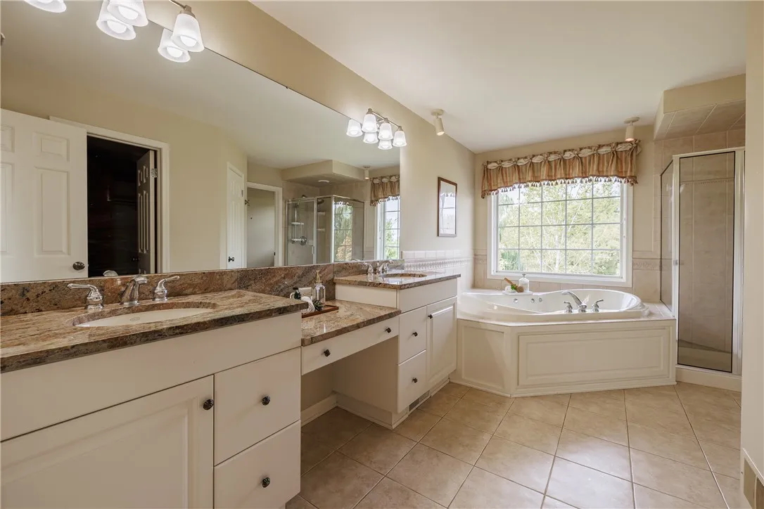 Spacious primary bathroom with tons of natural light, a dual sink/storage area and make-up area, a spa-like hot tub, a large shower and a privacy room with toilet.
