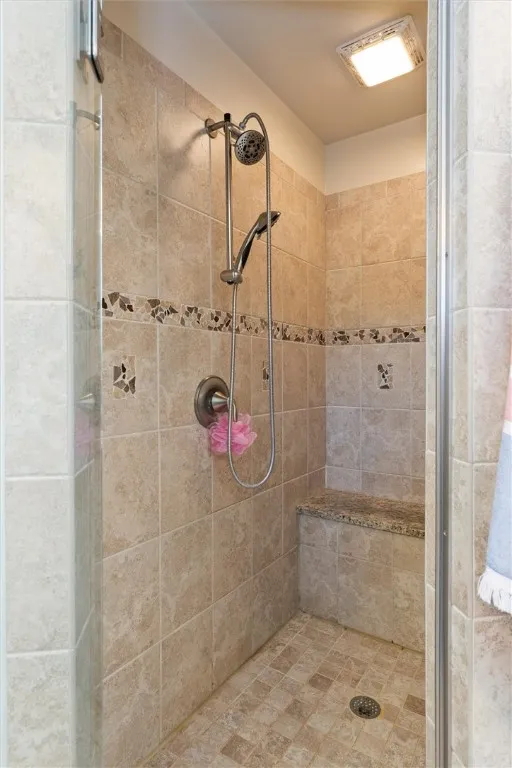 Step into the beautifully tiled walk-in shower, complete with a built-in bench and accent mosaic detailing — designed for comfort and timeless style.
