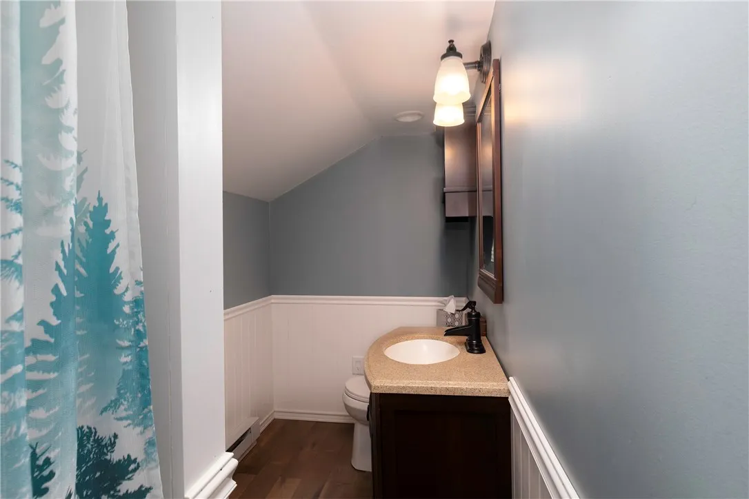 Updated bath with modern fixtures, beadboard wainscoting, and soft blue-gray walls. Features a solid-surface vanity, warm lighting, and a relaxing atmosphere with a touch of character.