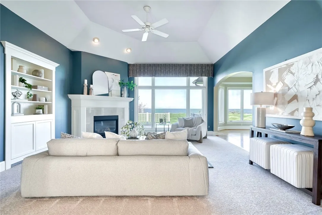 Great room with volume ceilings, anchored by a gas fireplace and built-ins—framed by that wall of glass!