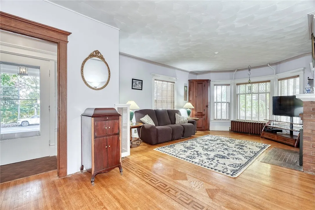 main family room opens wide — high ceilings, a brick fireplace, generous windows, and hardwood floors with inlaid detail.