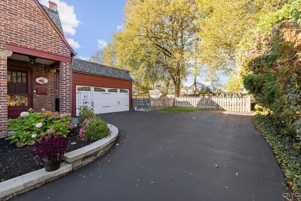 Retaining wall and two car garage with fenced in yard and mature trees.