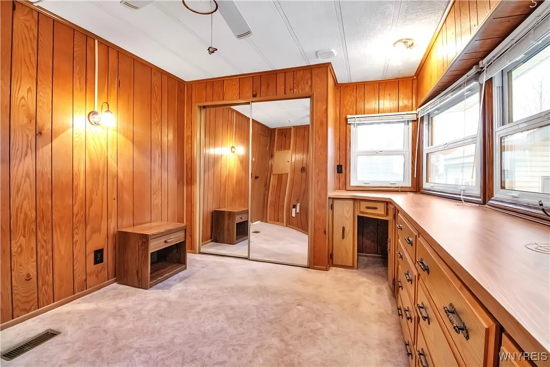 Back carpeted bedroom has sliding mirrored closet doors + wall sconce