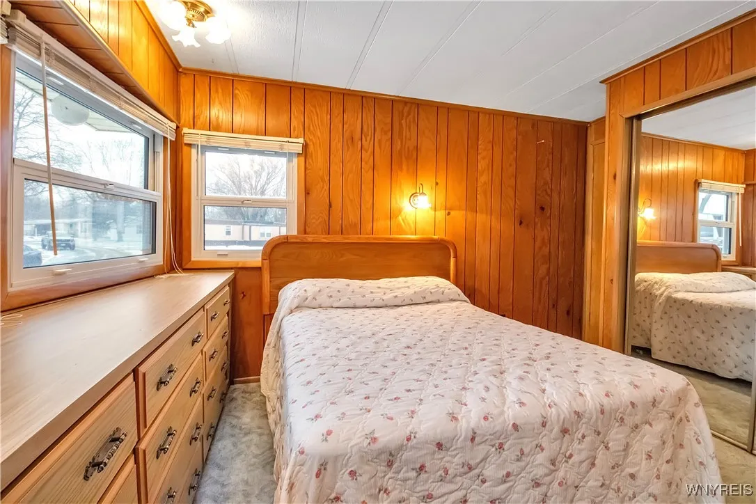 carpeted Primary bedroom has mirrored closet doors, ceiling lights + wall sconce