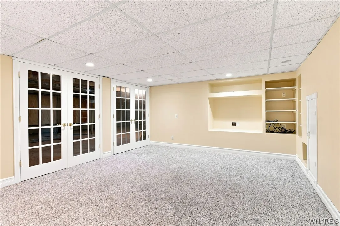 Basement/lower level  recreation space is fully carpeted and has double french door entry to an expansive storage/utility mechanics space