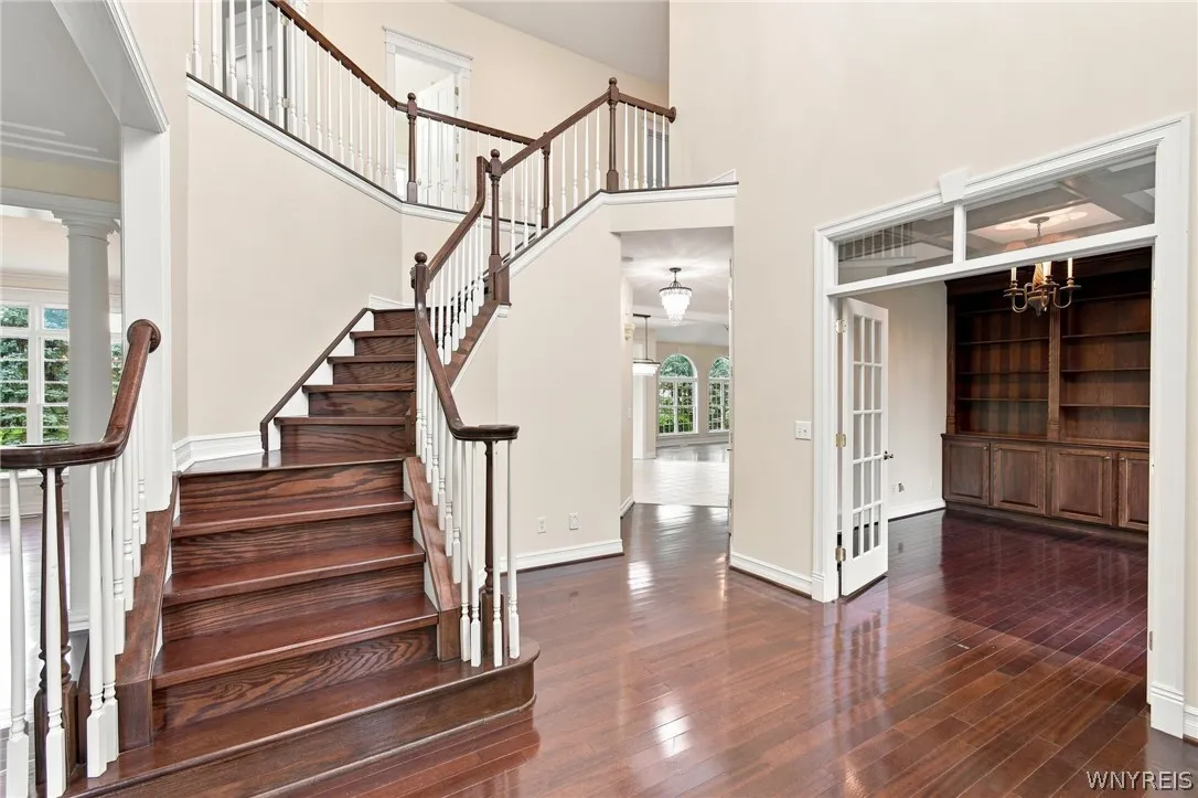 From the moment you step through the front door, this magnificent home captivates with a grand two-story entryway showcasing a soaring ceiling, a classic tier-candle chandelier, and a sweeping hardwood staircase with traditional wood banisters. Glistening Rosewood floors flow from the foyer into a sophisticated den behind elegant double French doors, complete with an old-world coffered ceiling and custom built-in bookcases.
The foyer acts as the perfect anchor for the home's exceptional main-level layout.