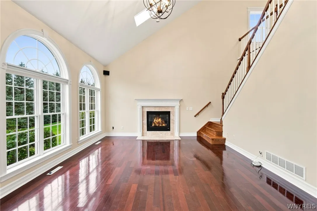 The family room flows seamlessly into the kitchen, anchored by magnificent Rosewood floors and a cozy gas fireplace. Overhead, an elegant orbital crystal chandelier highlights the dramatic cathedral ceiling, while spectacular triple picture windows with palladium accents fill the space with natural light. A second staircase offers convenient access to the upper level.
