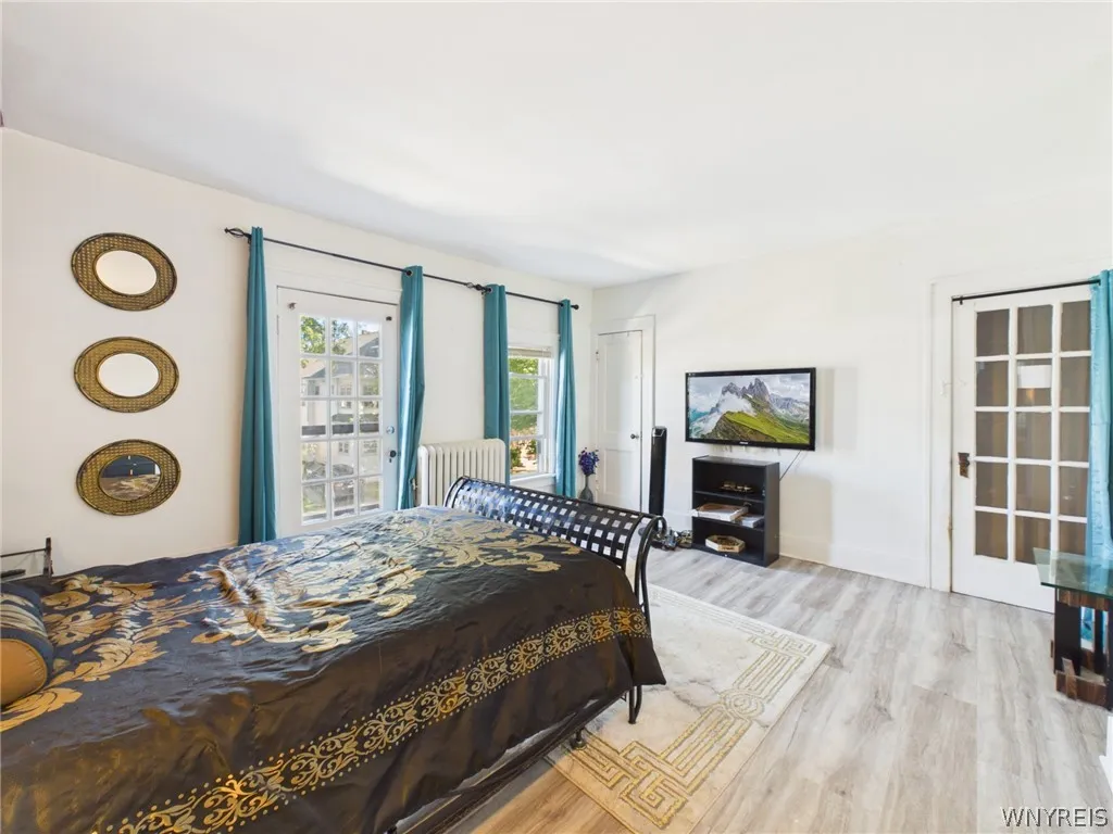 Primary Bedroom: A large bedroom with sloped ceilings, a painted accent wall, abundant natural light, wood-look flooring, a closet and a glass-paned exterior door.