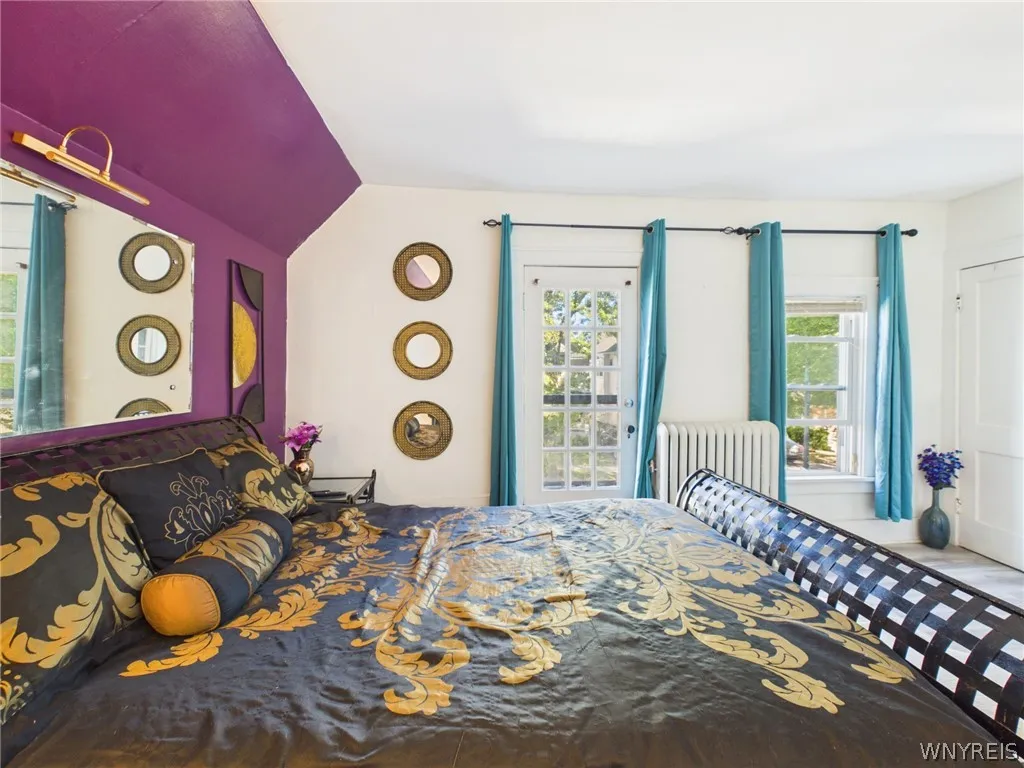 Primary Bedroom: A large bedroom with sloped ceilings, a painted accent wall, abundant natural light, wood-look flooring, a closet and a glass-paned exterior door.