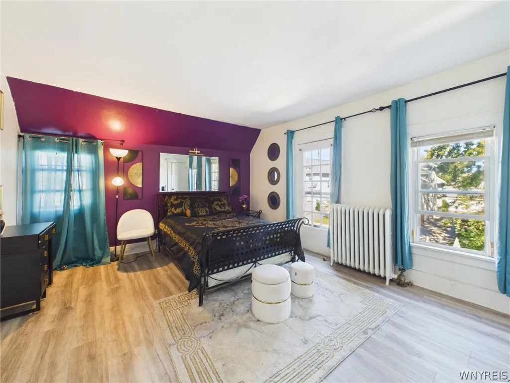 Primary Bedroom: A large bedroom with sloped ceilings, a painted accent wall, abundant natural light, wood-look flooring, a closet and a glass-paned exterior door.