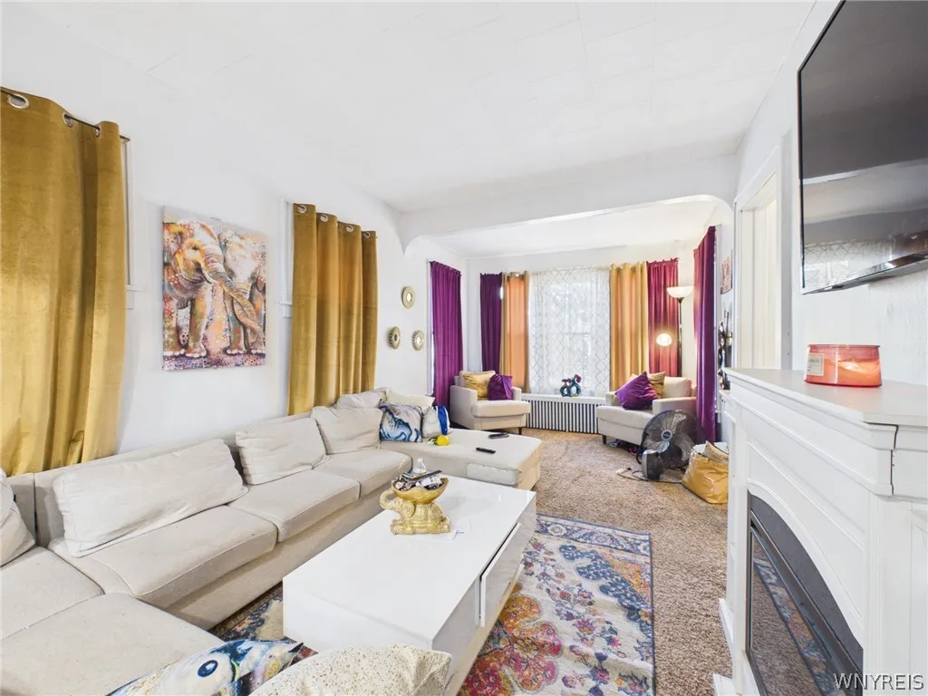 Living room: A large living room with a fireplace and white mantel, built-in shelves on both sides, and an arched opening to a bright front sitting area with a wall of windows.