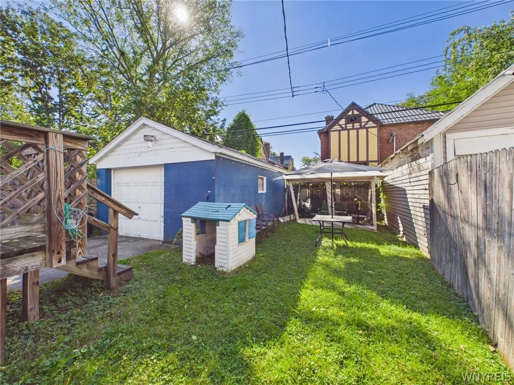 A fenced backyard with a detached garage, a patio table and a gazebo.