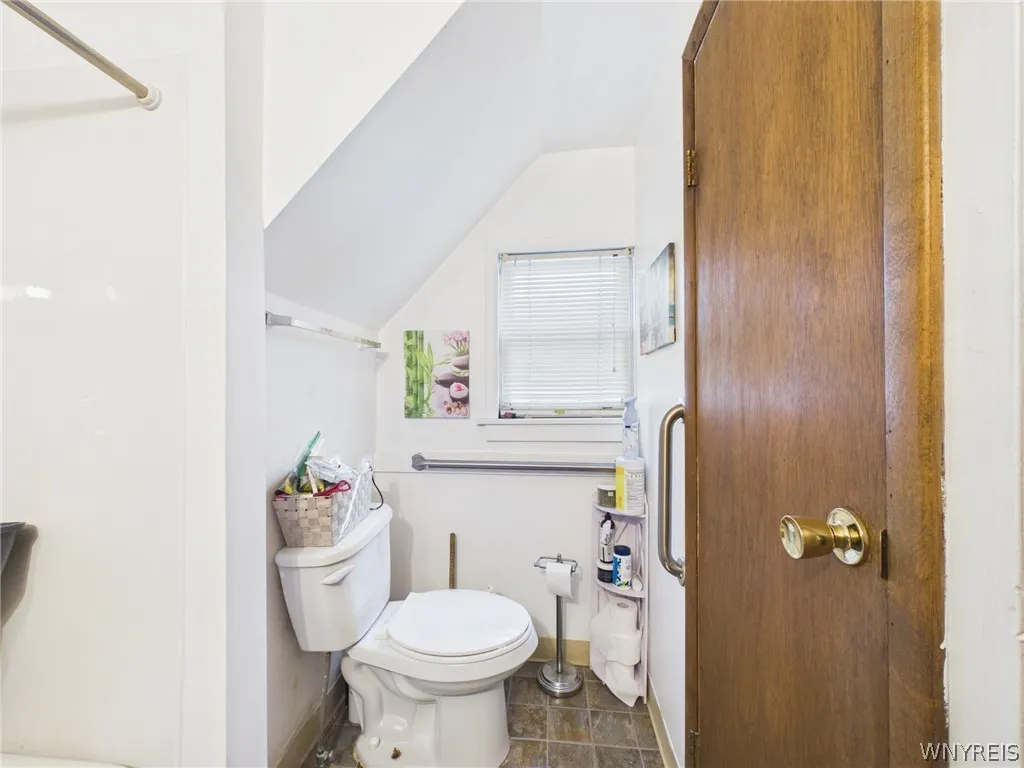 Bathroom, second angle: The toilet area has a sloped ceiling, a window and extra grab bars.