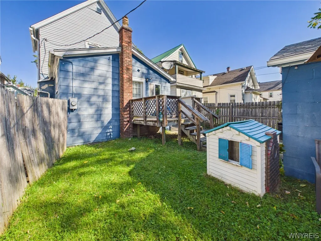 Backyard toward the house: A fenced lawn looking back at the rear deck and brick chimney.