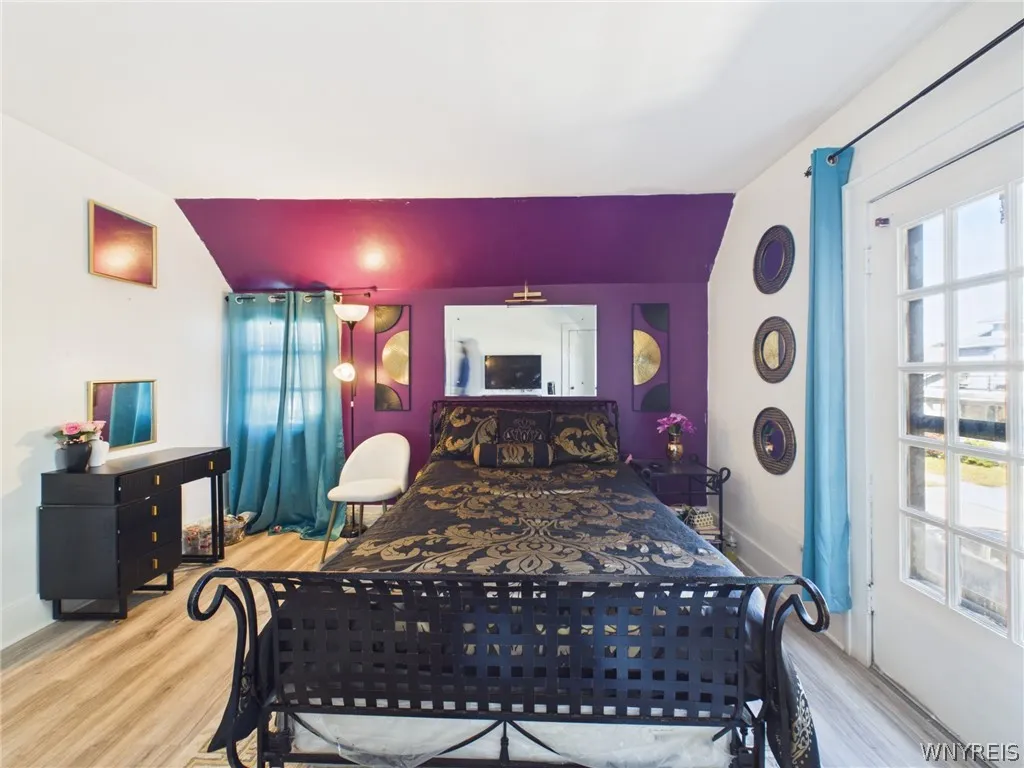Primary Bedroom: A large bedroom with sloped ceilings, a painted accent wall, abundant natural light, wood-look flooring, a closet and a glass-paned exterior door.