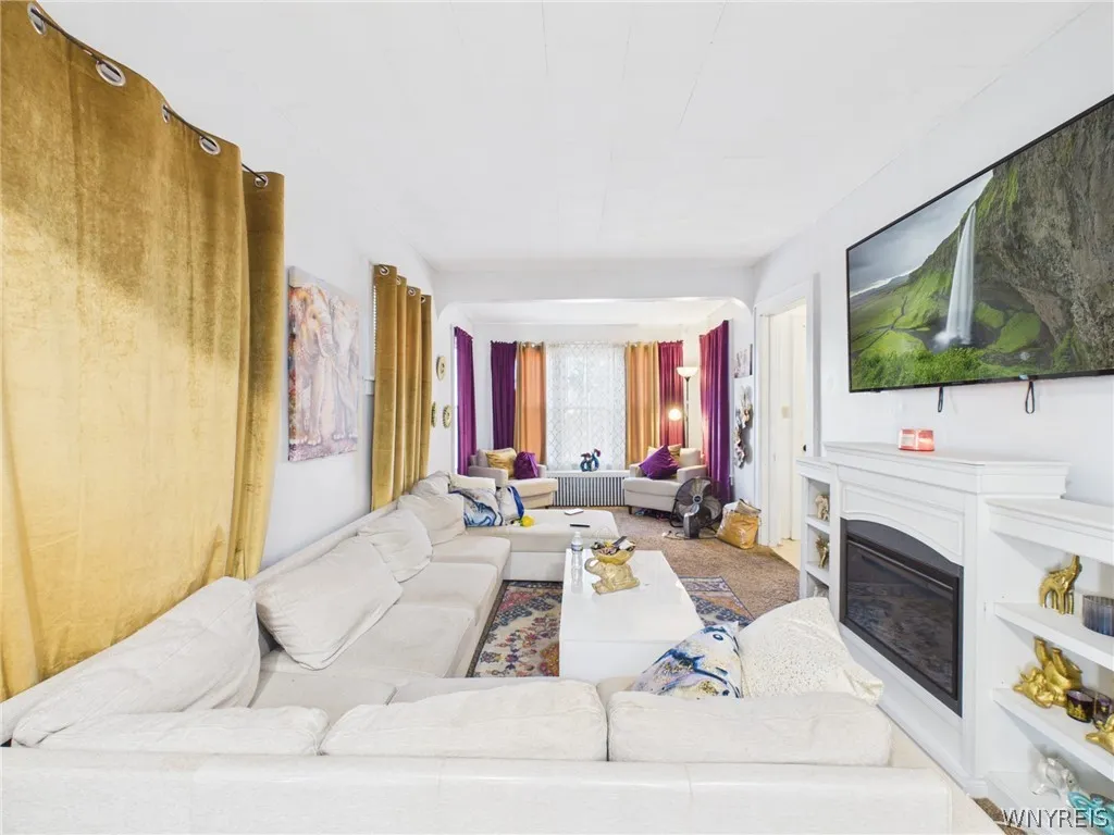 Living room: A large living room with a fireplace and white mantel, built-in shelves on both sides, and an arched opening to a bright front sitting area with a wall of windows.