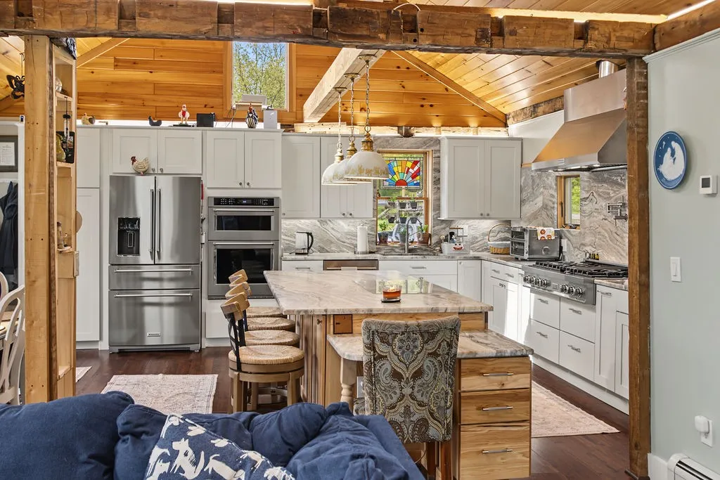 Exposed rustic wooden beams frame a well-appointed kitchen featuring high wood ceilings and premium stone counters.
