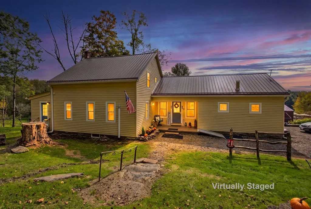 A metal roof and warm exterior lighting define this inviting country home at dusk.