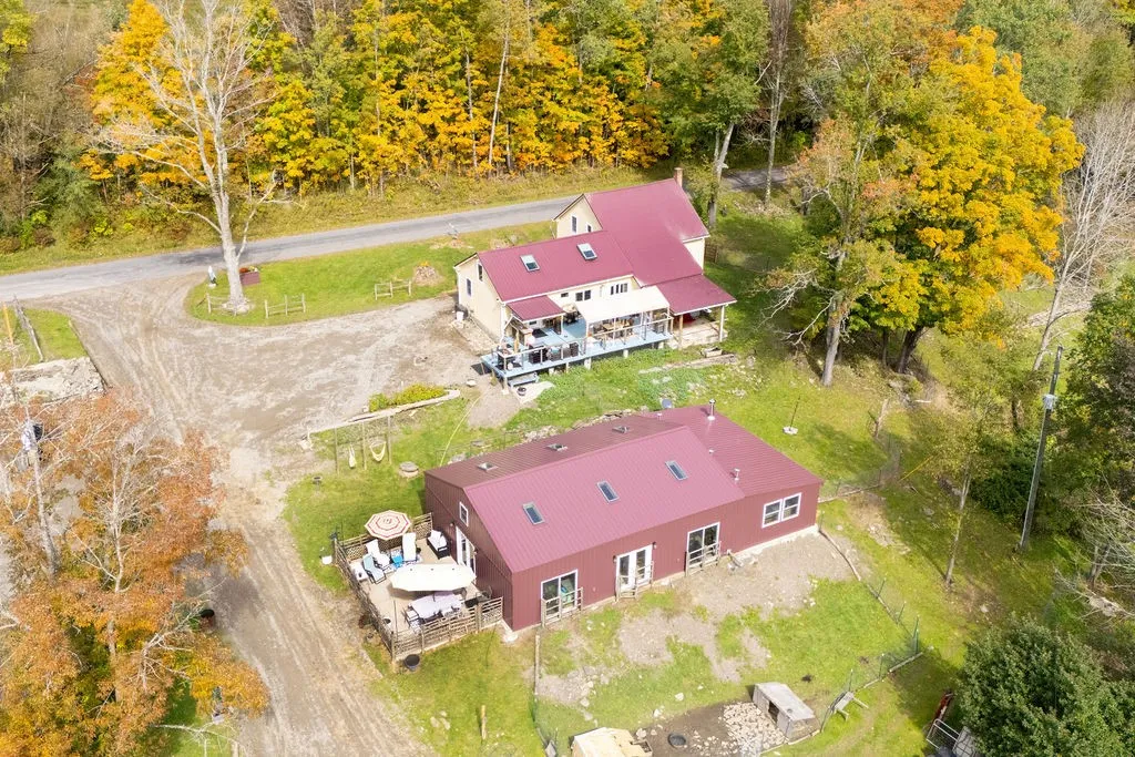 Aerial view captures two red-roofed structures nestled among dense autumn foliage and rolling green lawns.