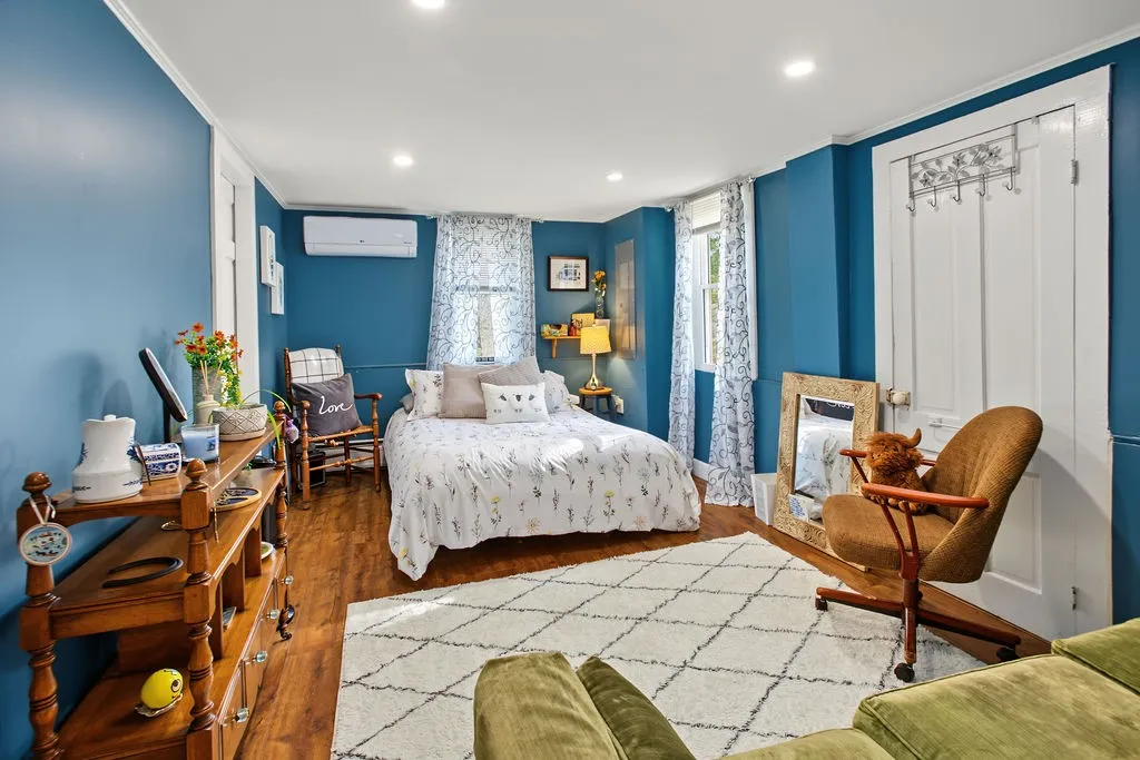 Rich wood flooring runs throughout this cozy bedroom featuring integrated recessed lighting.