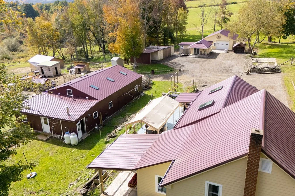 A sprawling rural homestead surrounded by mature trees offers multiple outbuildings and expansive lawns.