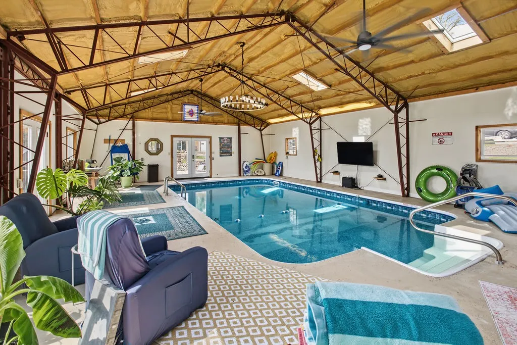 An indoor swimming pool rests under a vaulted ceiling with exposed metal trusses.
