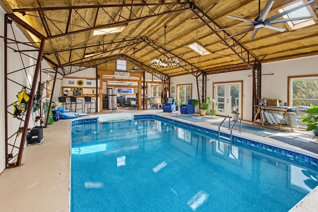 Industrial trusses and skylights frame a massive indoor pool house complete with an adjacent wet bar.