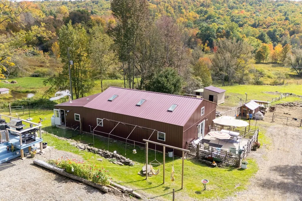 An aerial perspective captures the metal-roofed country residence surrounded by rolling forested hills.