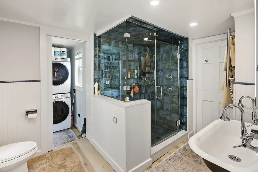 A glass-enclosed shower stall with blue tiling anchors this bathroom featuring light wood flooring.