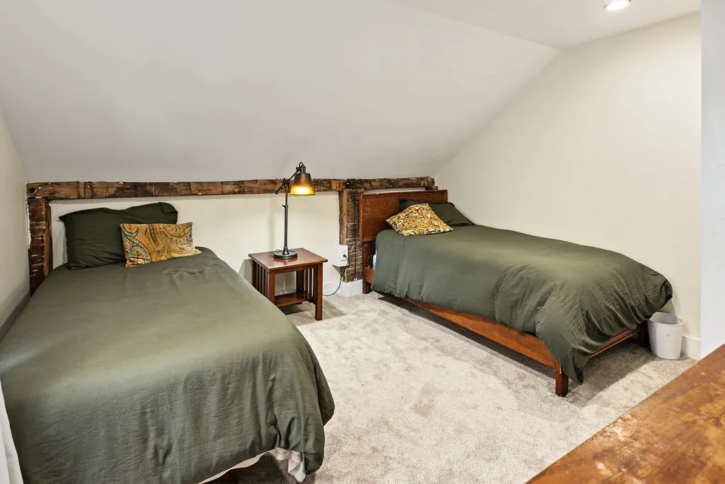 Exposed rustic wooden beams trace the sloped ceiling of this cozy carpeted space.