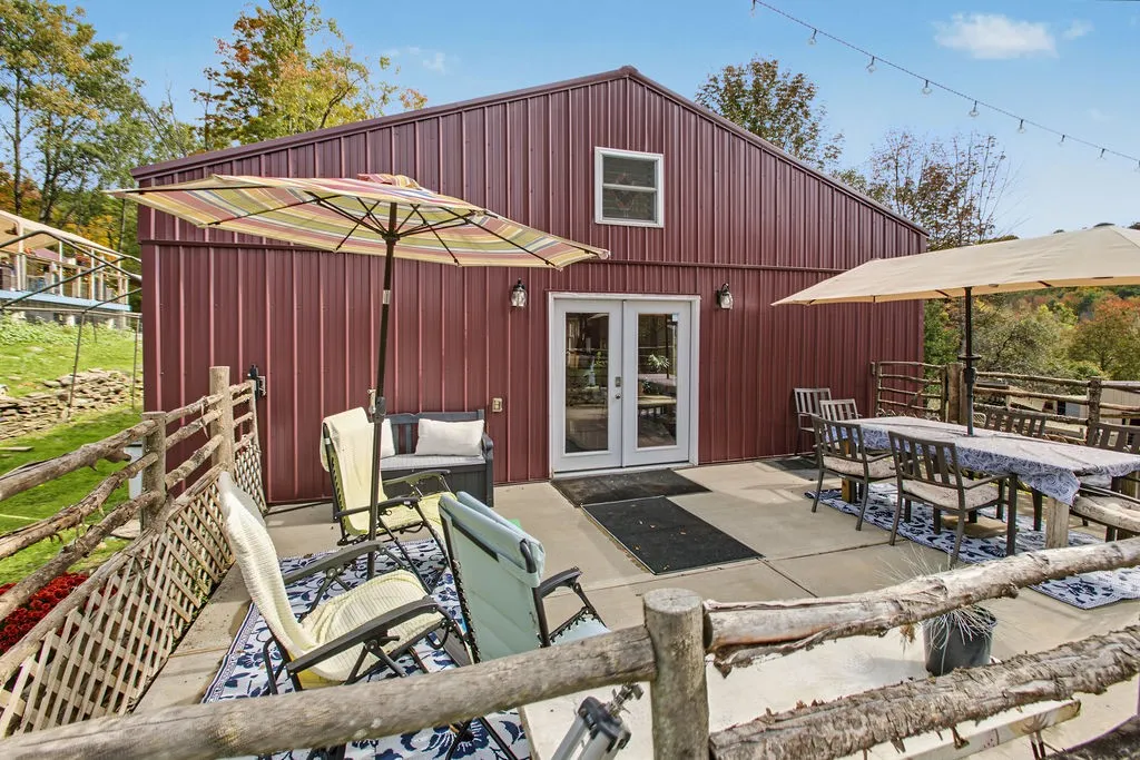 An inviting concrete patio borders the rustic metal outbuilding, ideal for outdoor gatherings.