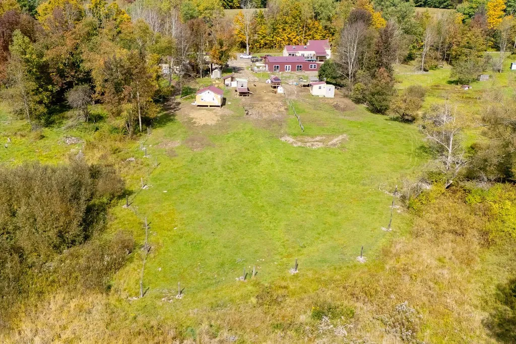 An aerial perspective reveals a vast grassy clearing bordered by mature trees and outbuildings.