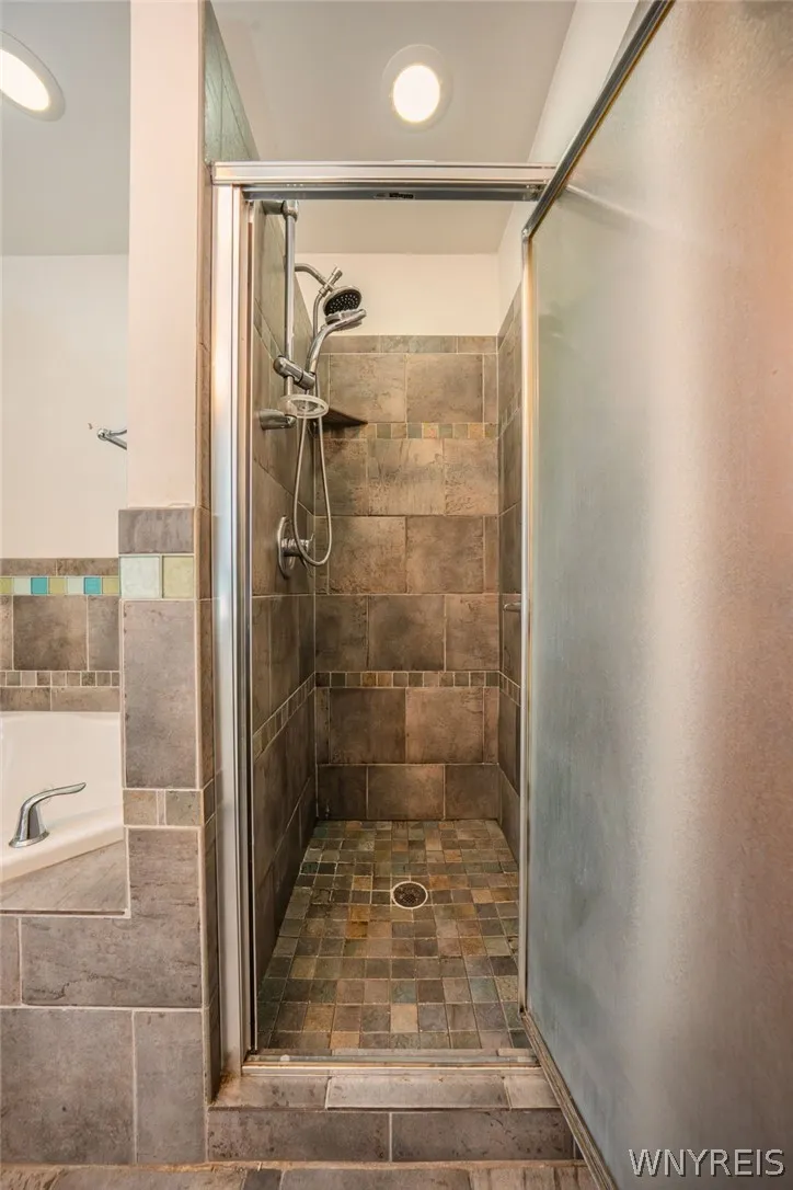 A glass-enclosed shower showcases rich stone tiling from floor to ceiling.