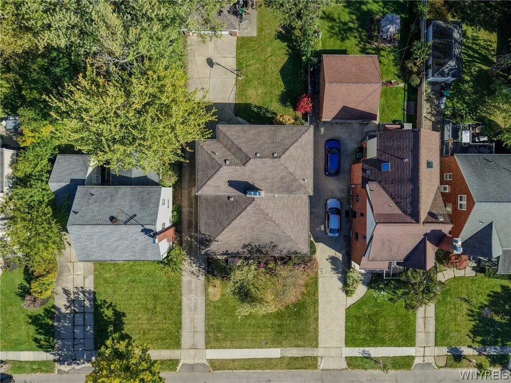 An aerial perspective showcases the shingle roof, paved driveway, and lush surrounding greenery.