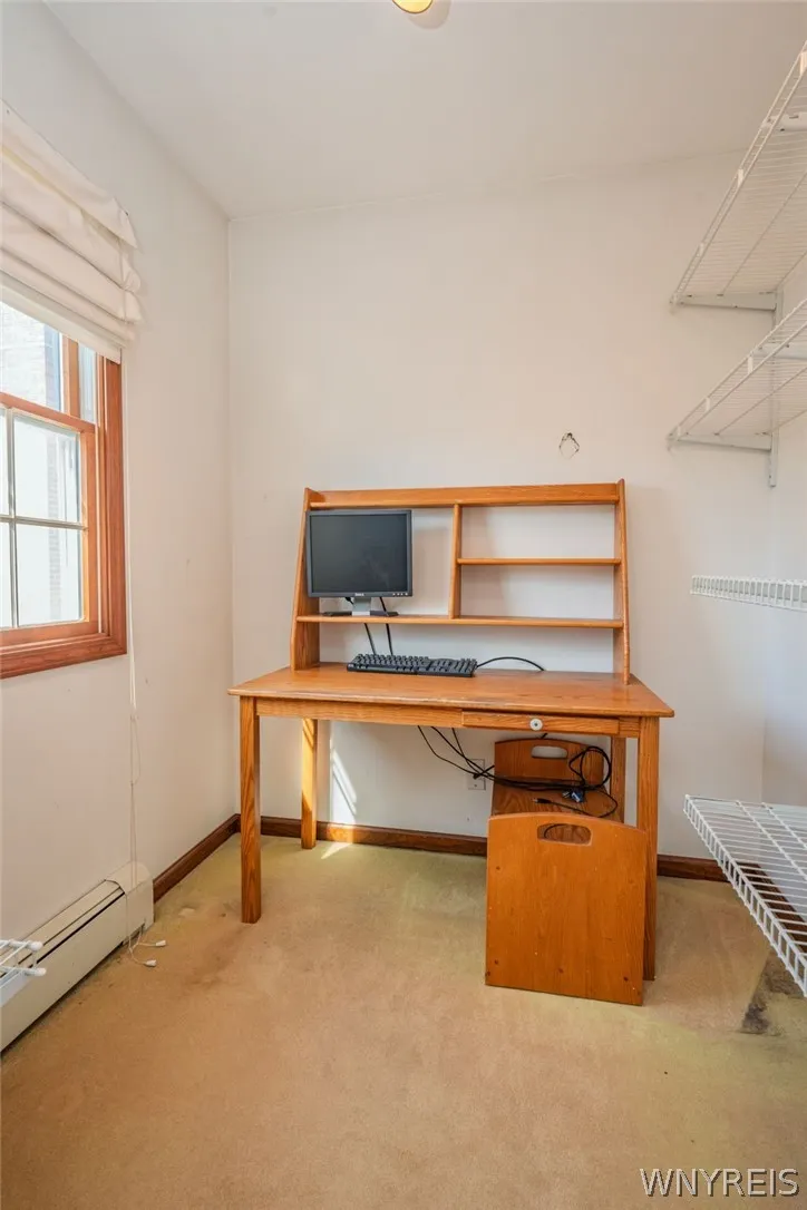 A cozy home workspace offers built-in wall shelving, a wood-trimmed window, and wall-to-wall carpeting.