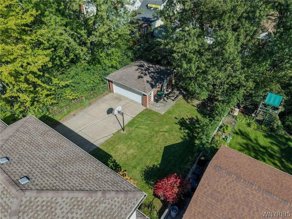 Mature trees frame a detached garage and concrete driveway with an integrated basketball hoop.