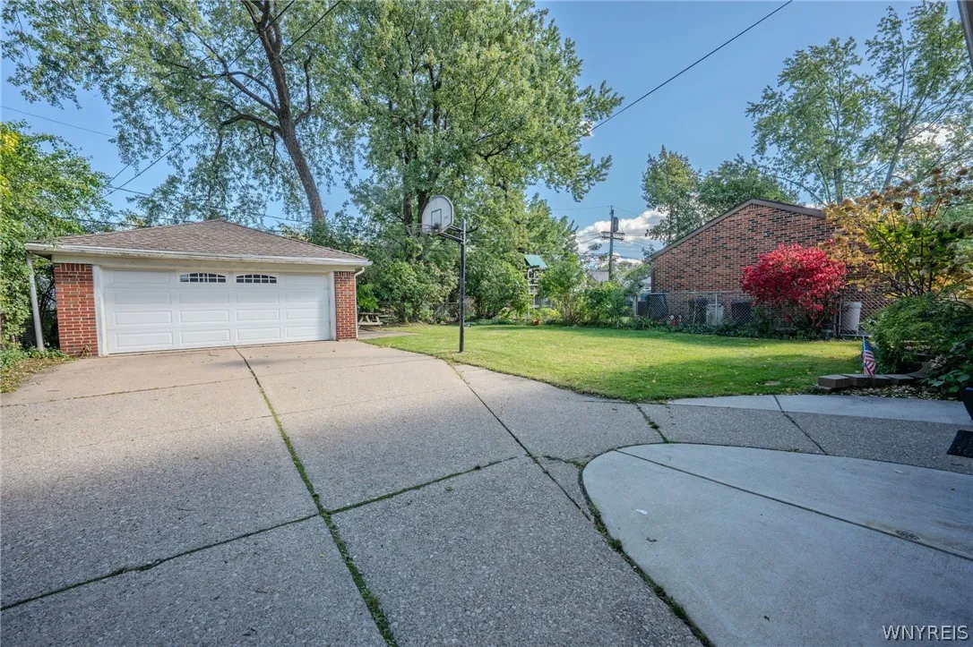 Mature trees frame a wide concrete driveway leading to a detached brick garage.
