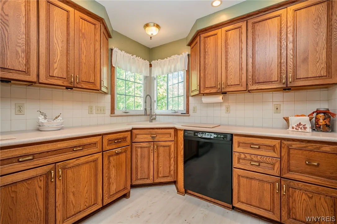 Rich wood cabinetry surrounds a corner sink under windows framing leafy green outdoor views.