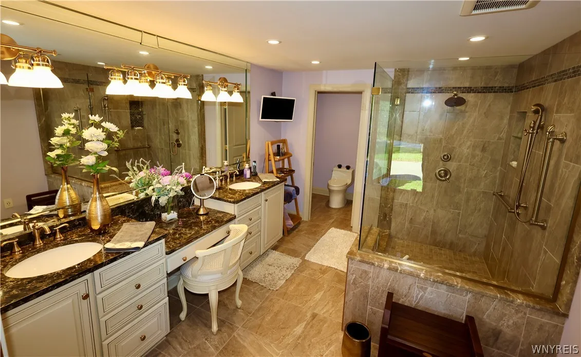 Granite counters and a spacious glass-enclosed shower highlight this tile-floored bathroom.