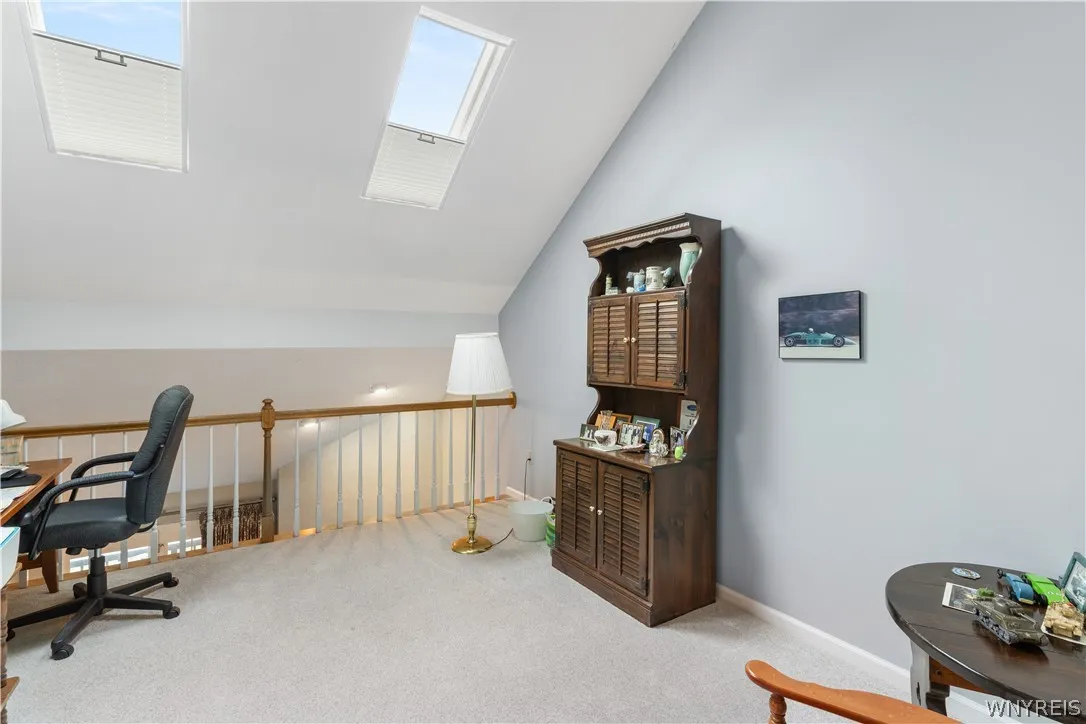 Natural light pours through dual skylights in this versatile upper-level loft area with carpeted floors.