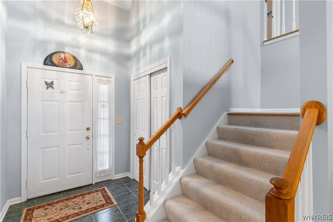 An inviting entrance foyer reveals tile flooring and a carpeted staircase with wood handrails.