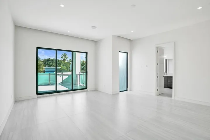 Primary Bedroom — Oversized suite with high ceilings, two walk-in closets, and an east-facing covered balcony large enough to serve as an outdoor living room. Balcony includes TV and spa connections and overlooks the pool.