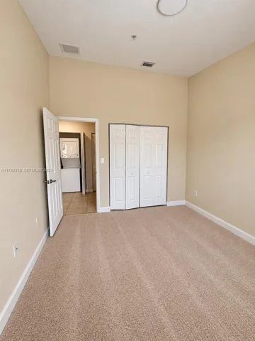 Neutral-toned interior room featuring high ceilings, wall-to-wall carpeting, and a bifold door closet